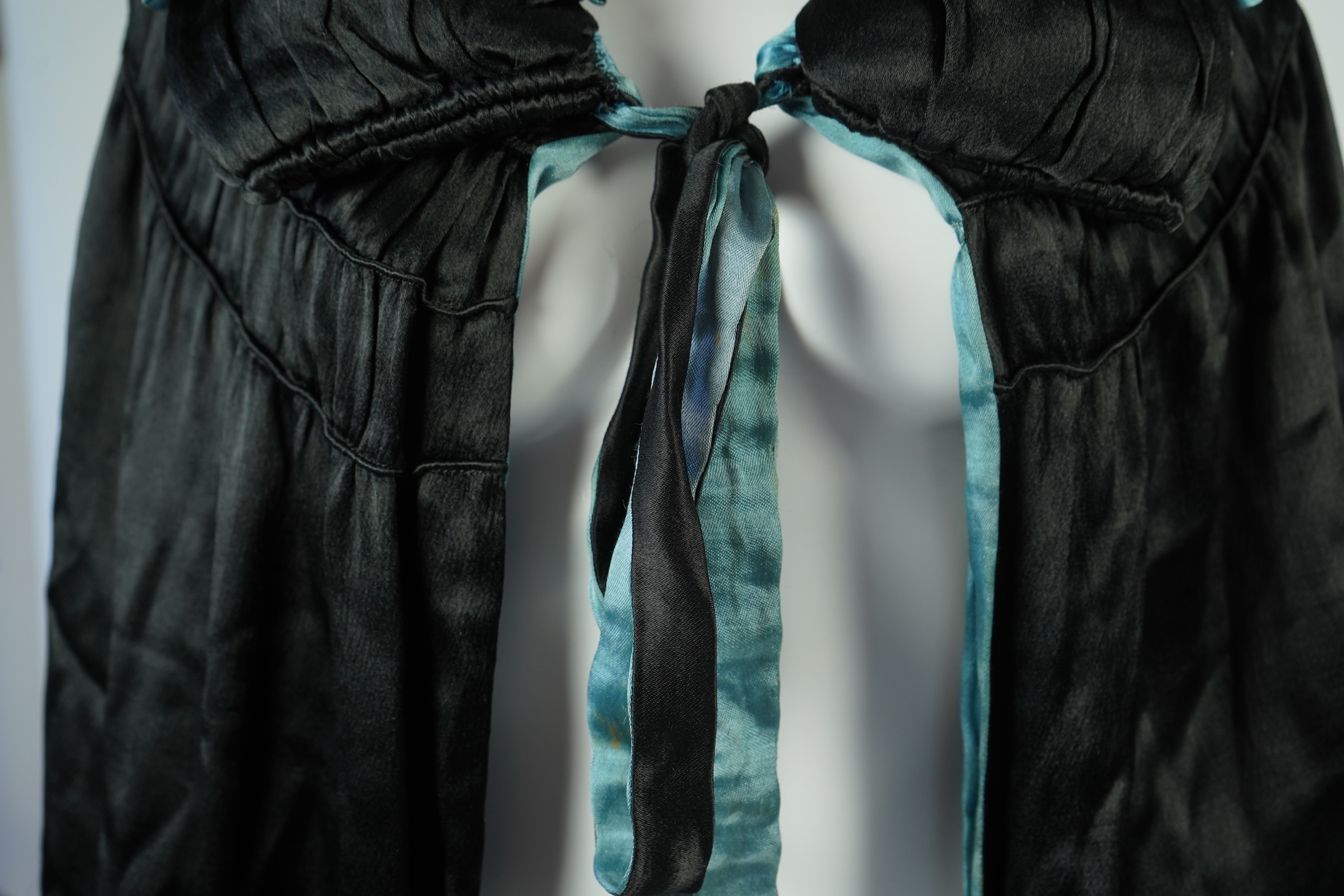 A 1920's ladies blue lined, black silk opera cape. Designed with a rushed ornate collar and scalloped and fringed lower edge. 95cm long fron neck to base. Condition - stained near the front edge, possibly removable with